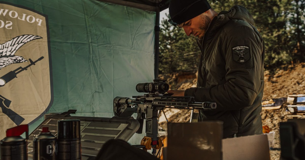 Instruktor MyMan Team montuje lunetę na karabinku AR-15 przy stanowisku polowym
